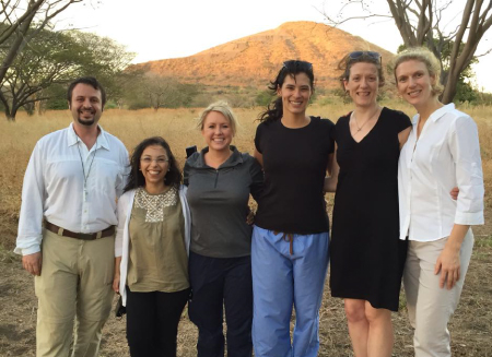 The group from the 2015 trip, 6 people standing in front of a mountain in the background with wind blowing