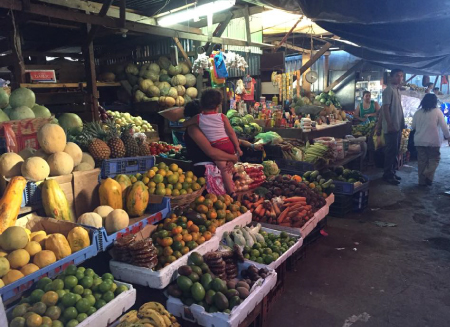 A fresh fruit and vegetable Market in Managua, with tarps overhead and a vendor holding a young child in her arms