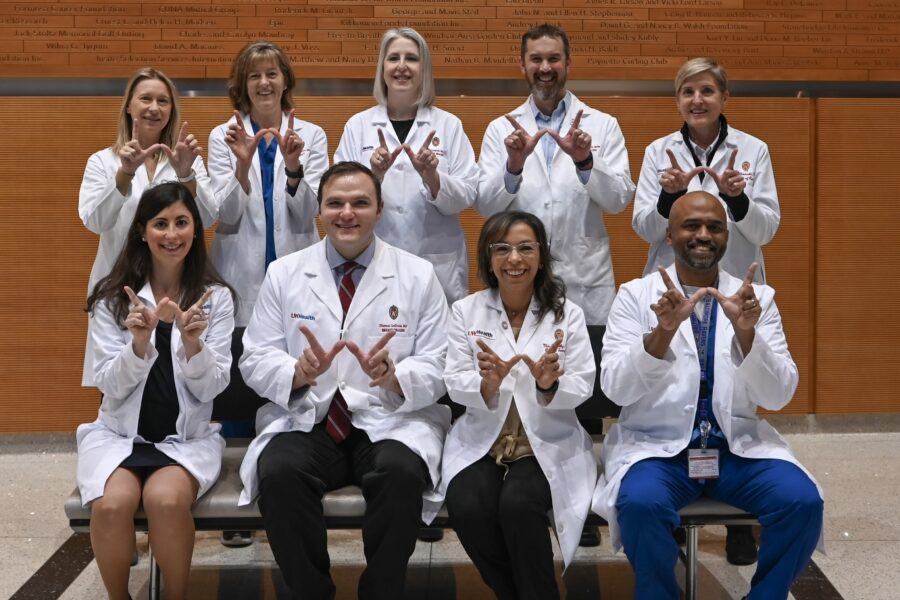 Photo of nine physicians wearing white coats and making the Wisconsin