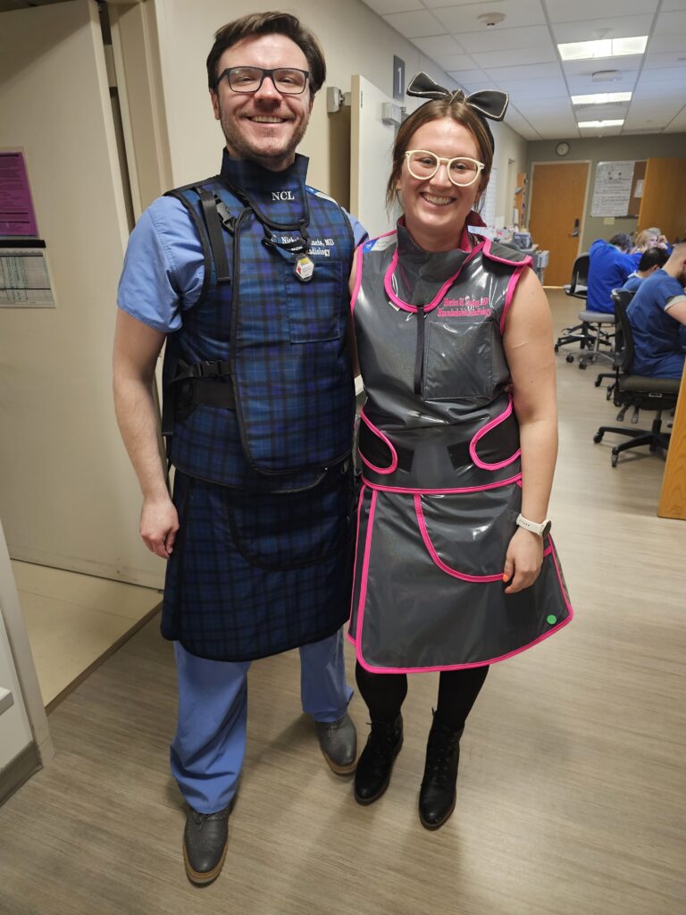 From left to right: Nicholas Laucis, MD and Monica Cooley, MD don protective lead aprons and thyroid guards for their demonstrations at the spinal intervention station.