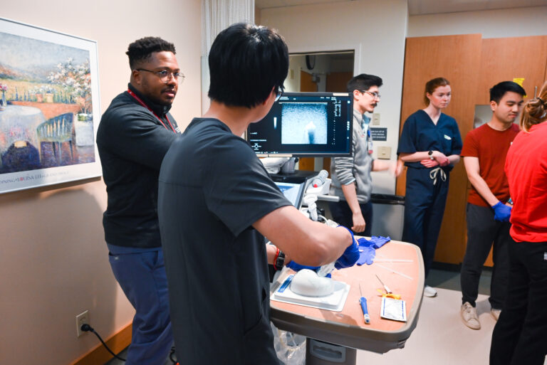 Fellow Lewis Jordan, MD assists a medical student obtaining a sample for biopsy from a breast training model.