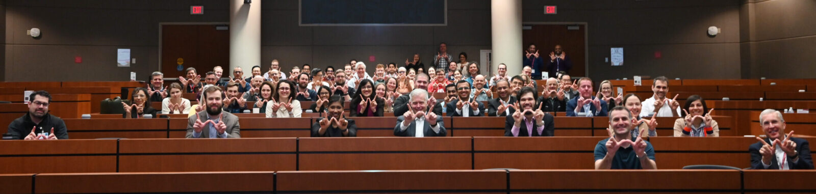 Scott Reeder and faculty sitting in lecture room holding "W" sign