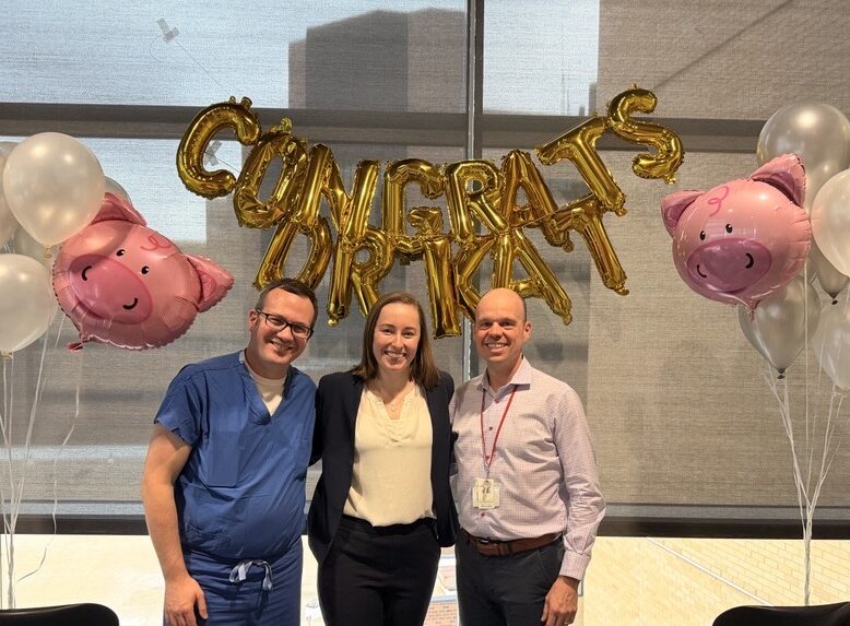 Two men and a woman pose together surrounded by ballons that read congratulations Dr. Kat.