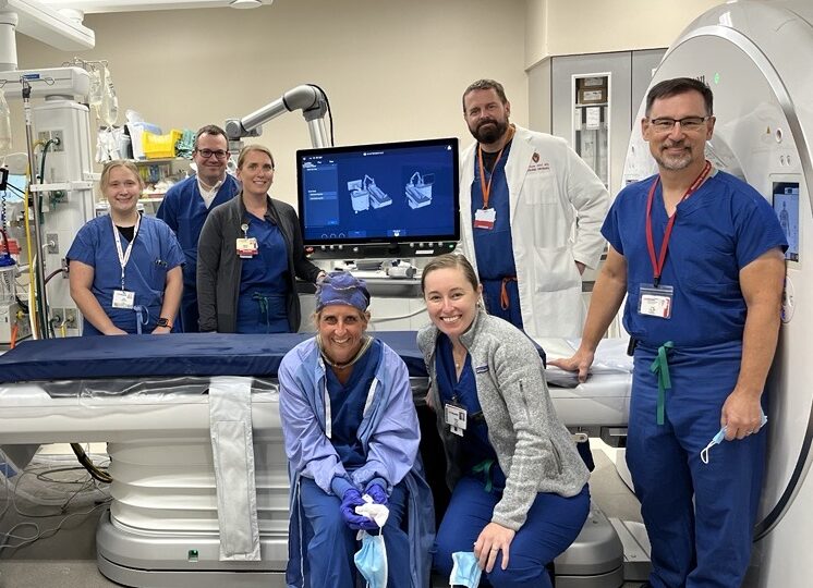 Seven medical staff members pose with medical equipment in a procedure room, celebrating.