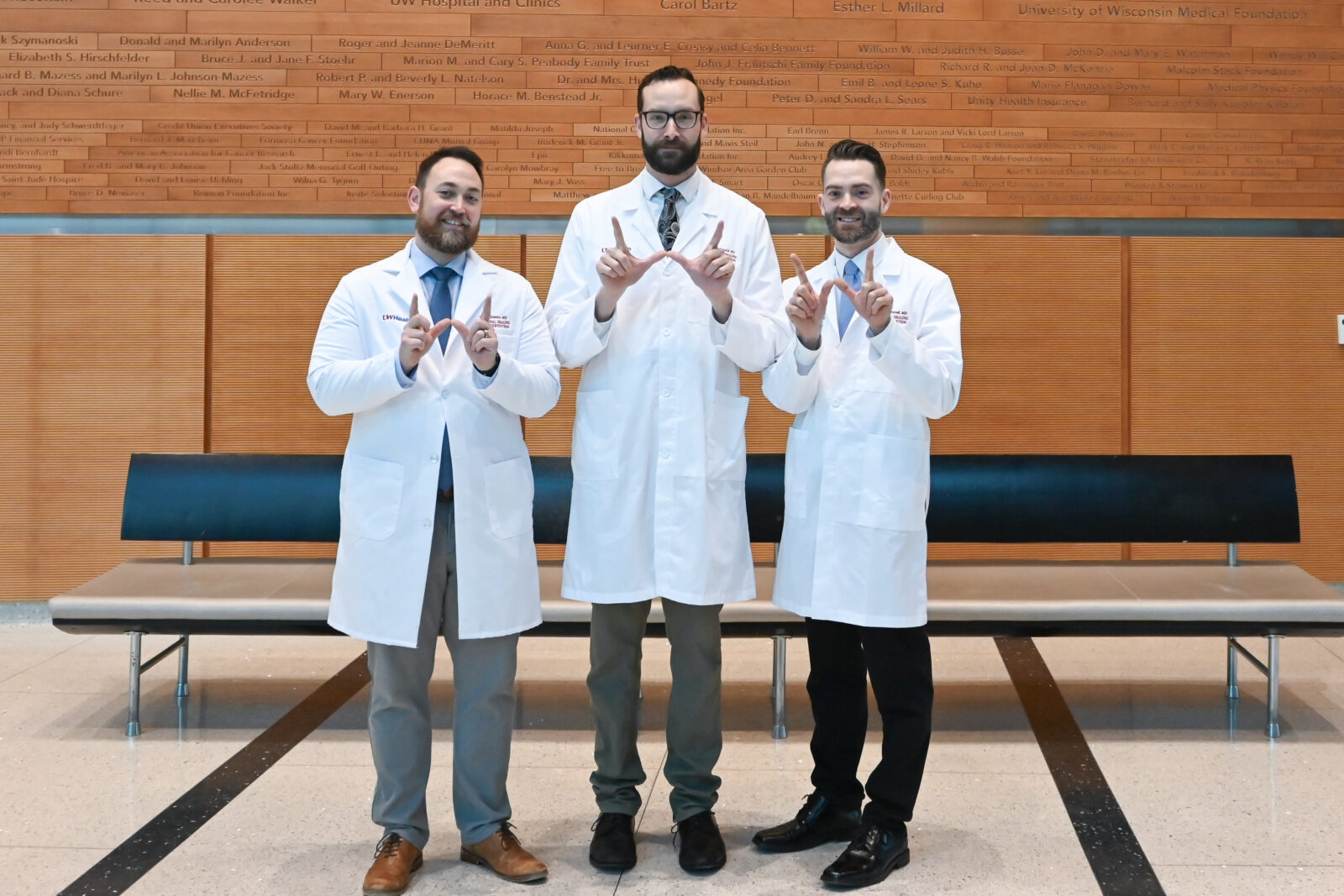A group photo of medical professionals standing in white coats. They are forming a 'W' with their hands.