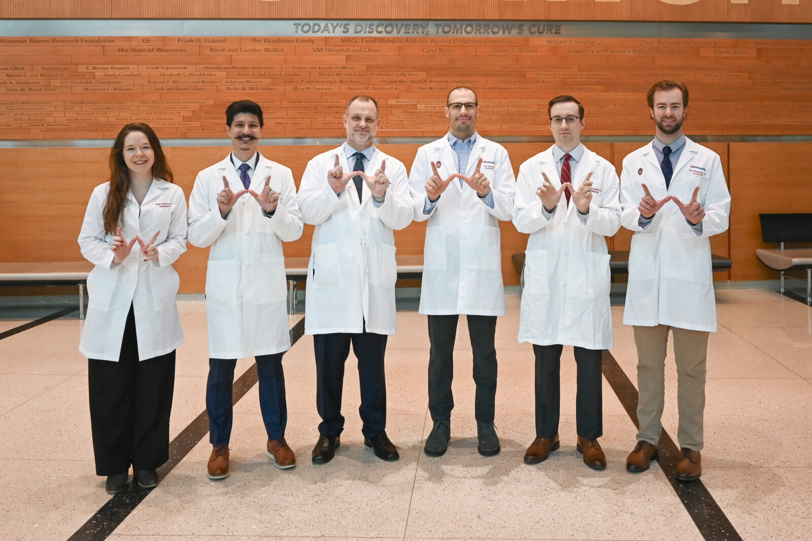 A group photo of medical professionals standing in white coats. They are forming a 'W' with their hands.