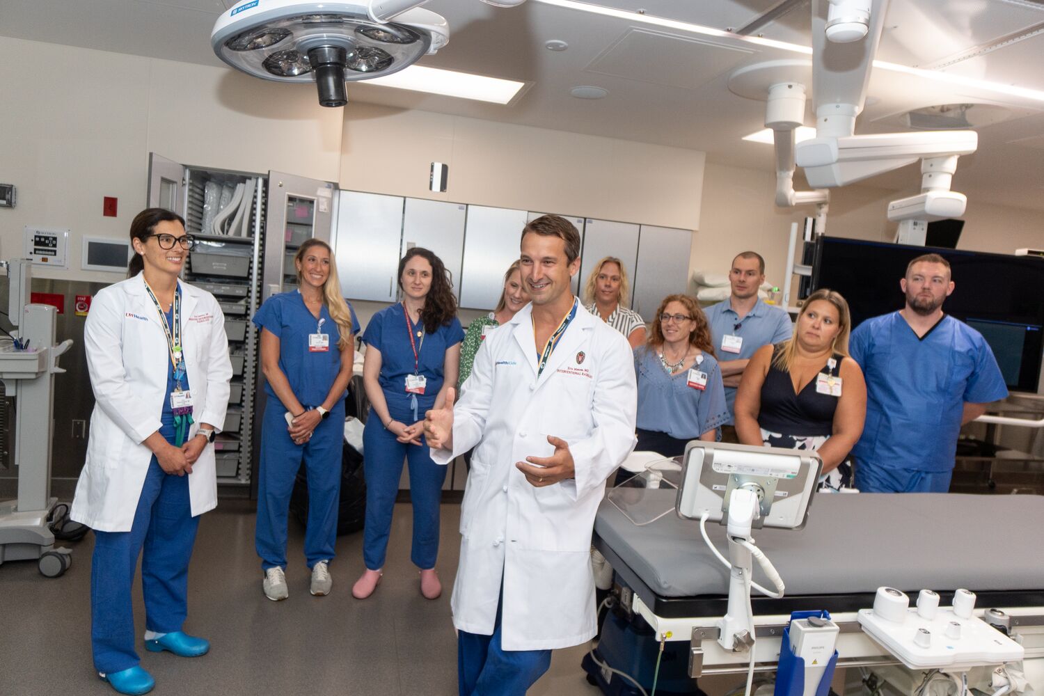 A doctor in a white coat talks with a group of people in an imaging suite.