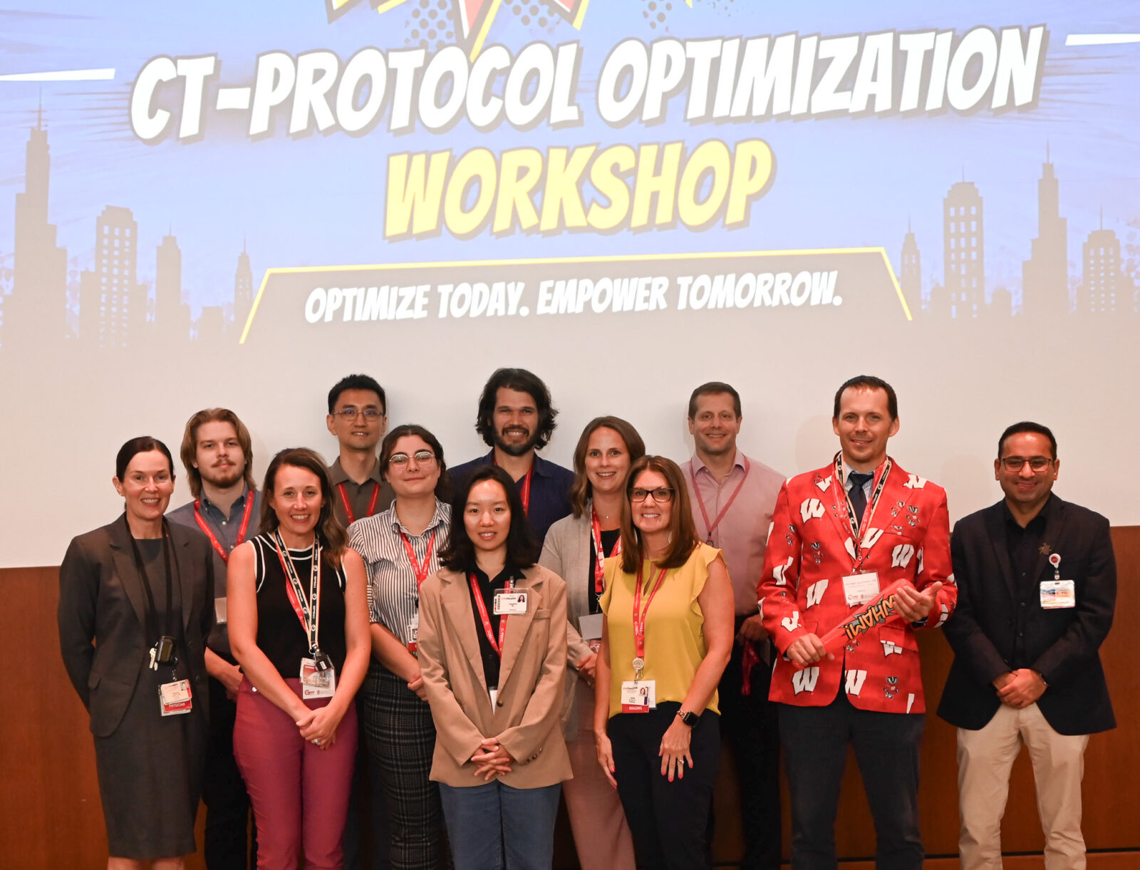 A group of people pose for a photo in front a screen that reads CT-Protocol Optimization Workshop.