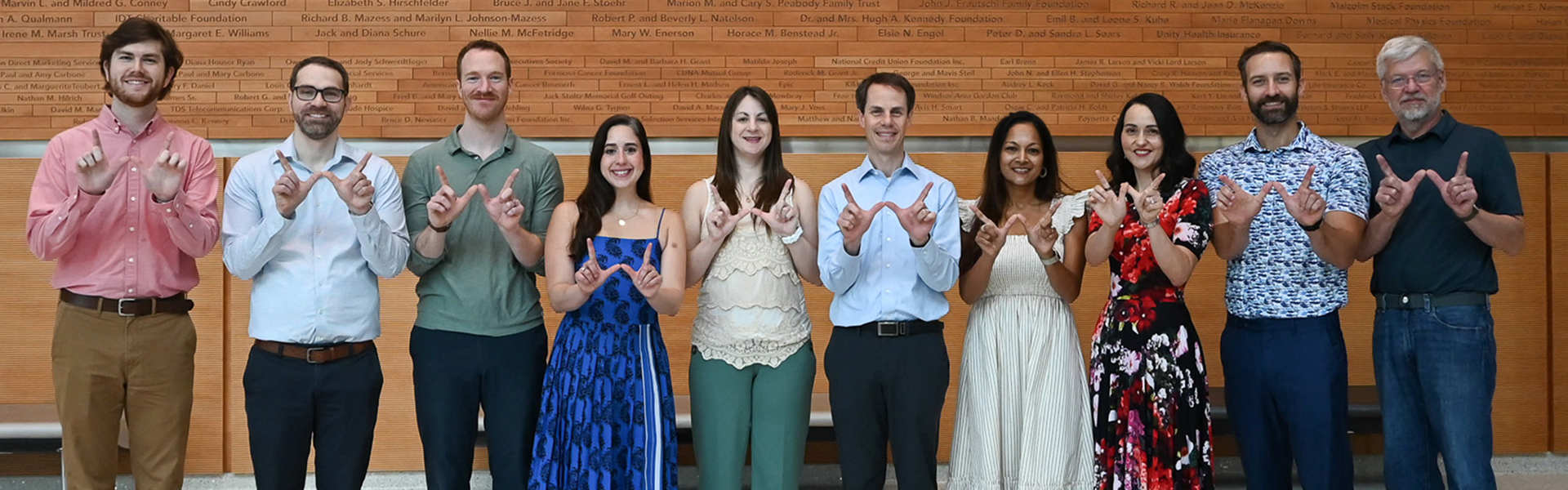 A group of 10 people stand in a line and each make a W for Wisconsin with their hands.