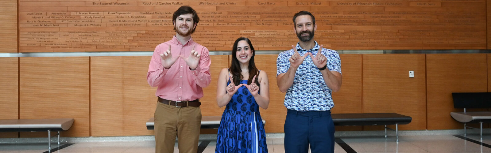 A group of three people stand in a line and each make a W for Wisconsin with their hands.